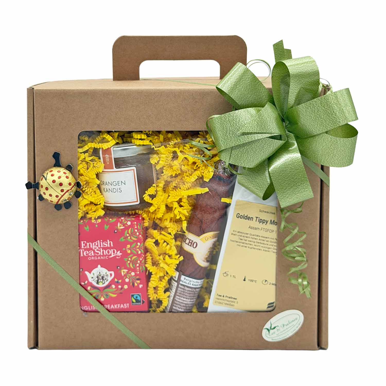 Geschenkbox mit English Tea Shop-Tee, orangefarbenem Kandiszucker, Schokolade und Assam-Schwarztee, dekoriert mit einem grünen Band.